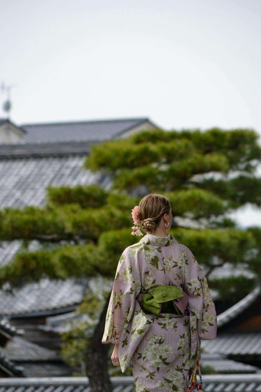 Woman in a floral kimono walking past a pine tree in Kyoto